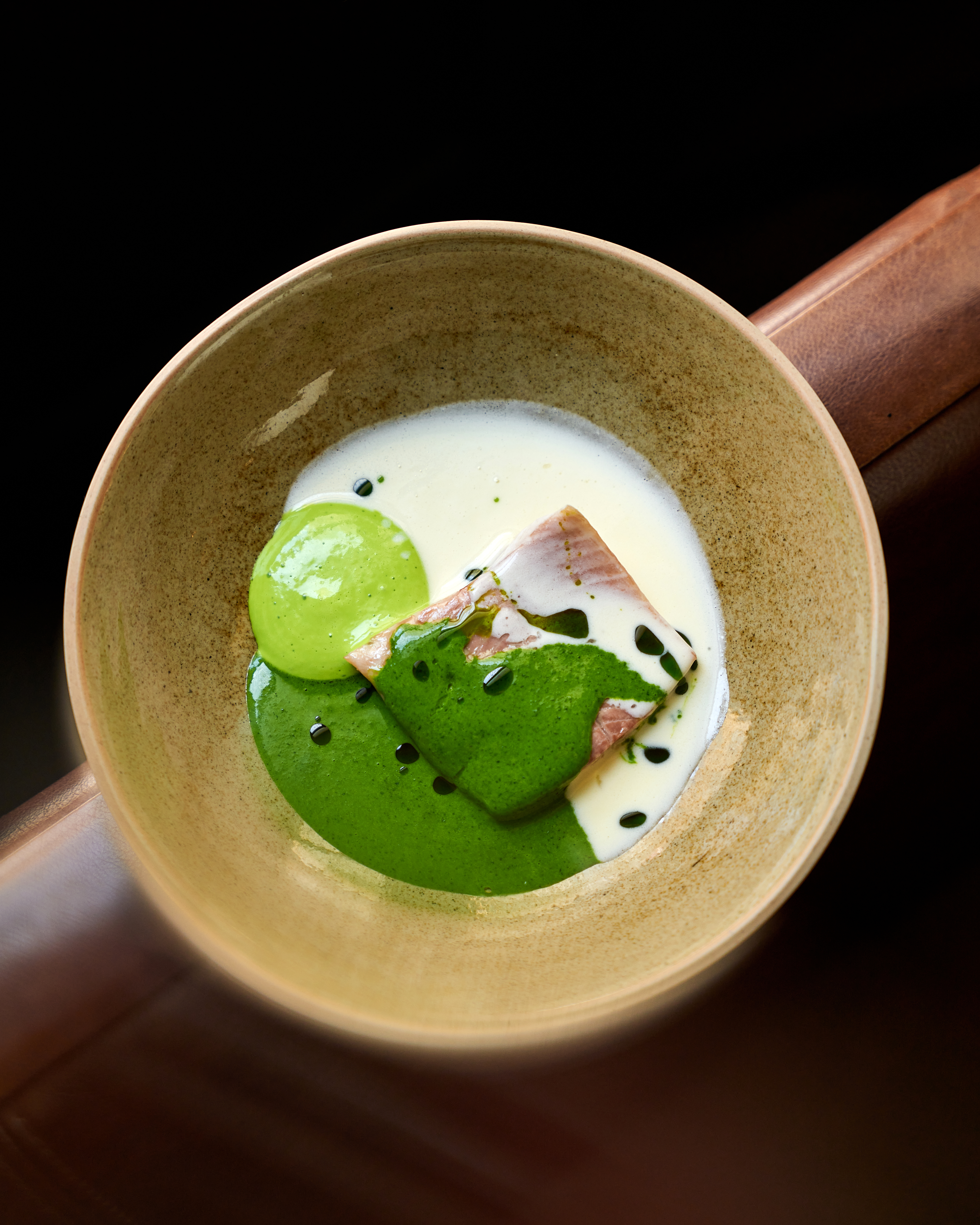 Portion of fish with green sauce and light foam in a ceramic bowl.