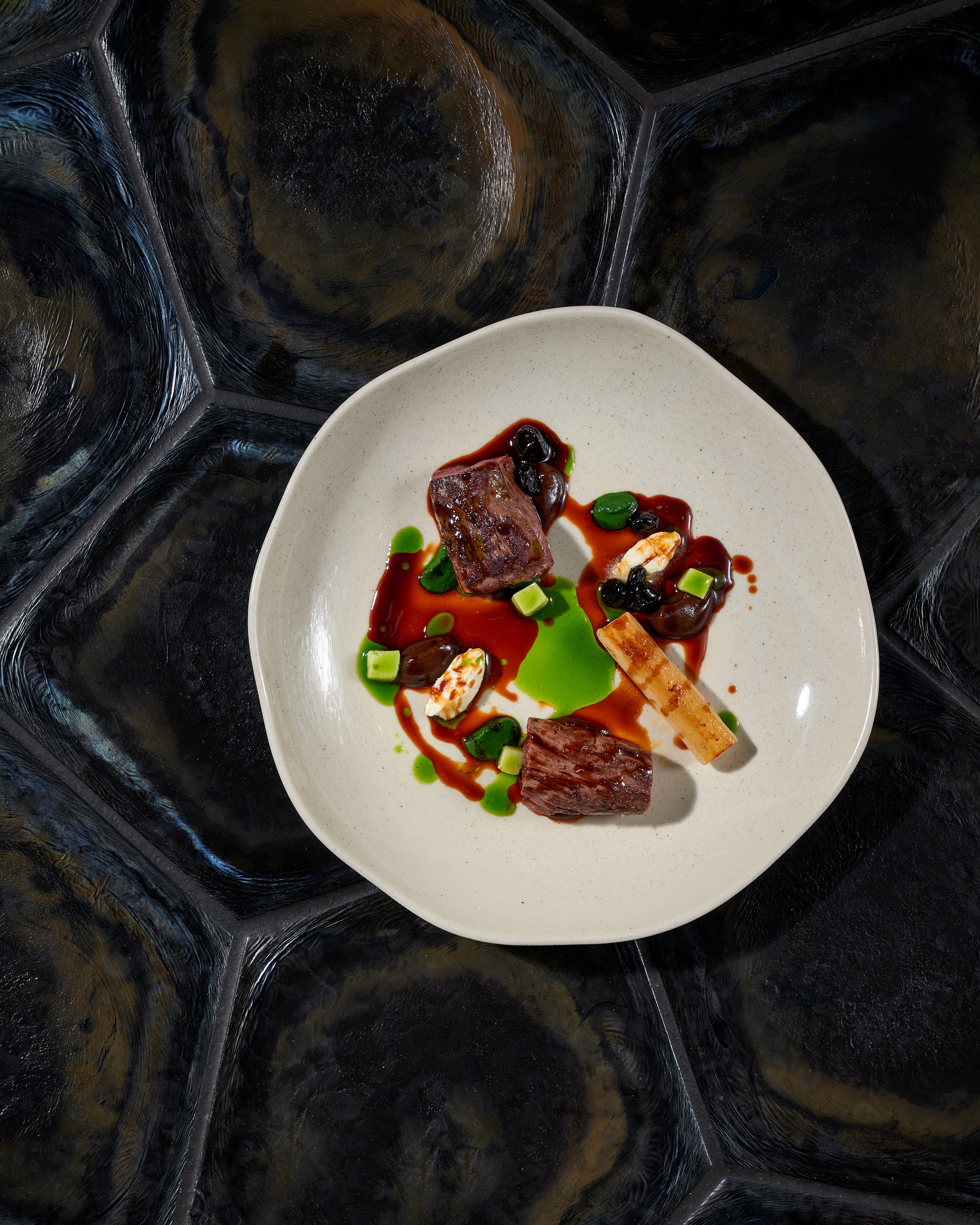 Grilled meat with bone, green sauce and accompaniments on a plate.