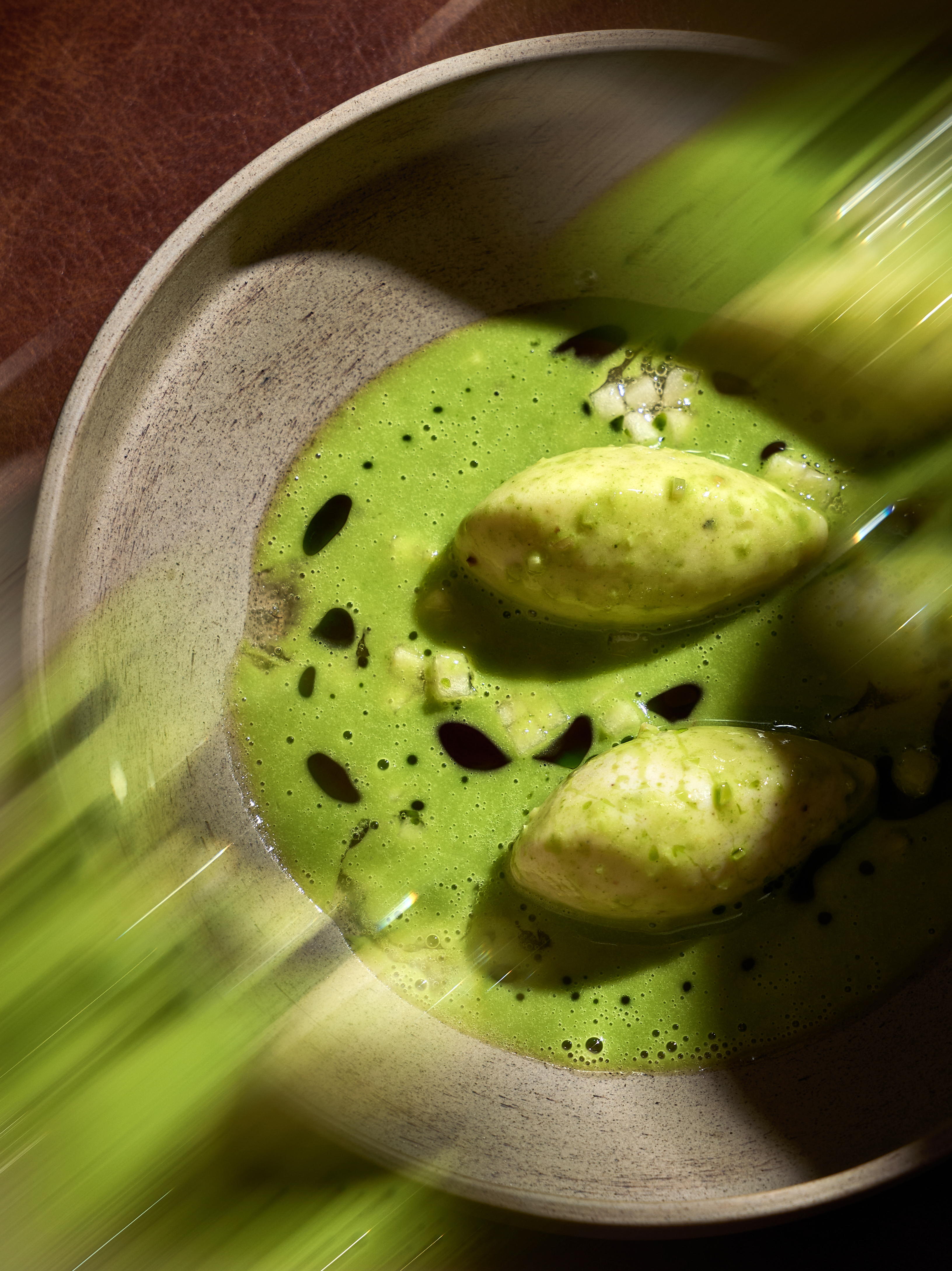 Green sauce with two dumplings and drops of oil in a ceramic bowl.